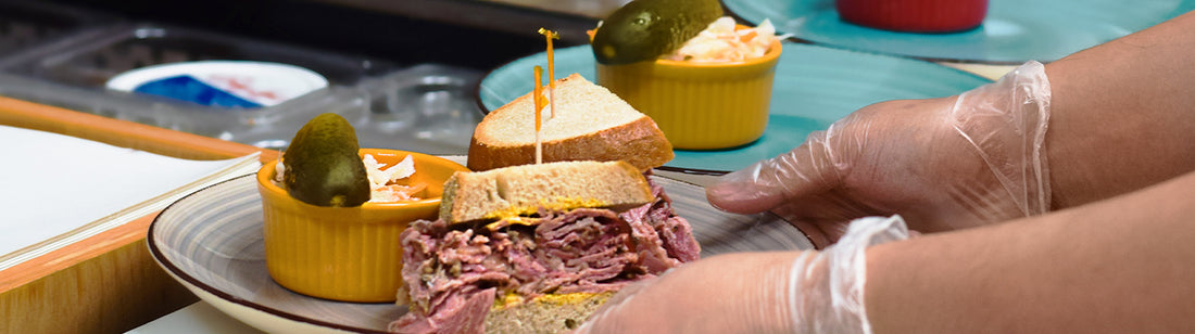 person placing sandwich onto a plate while wearing vinyl gloves