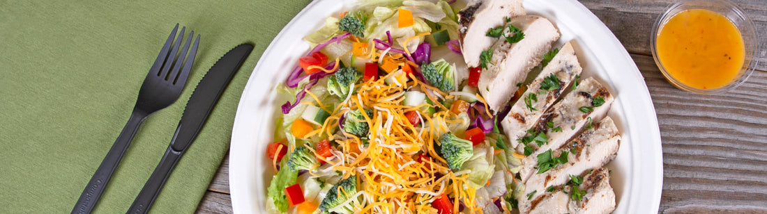 pla cutlery next to a molded fiber plate with salad on it with a pla portion cup on the side for the salad dressing