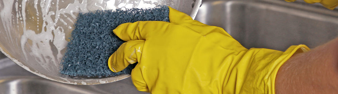 person wearing yellow rubber glove and cleaning a bowl with a scouring pad