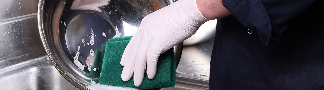 somebody washing a steel bowl with a green scouring pad