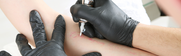 artist wearing black nitrile gloves and tattooing an arm
