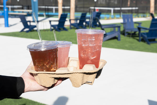 Person carrying drinks in a fiber tray. the drinks are in clear cups with clear compostable cellulosic straws