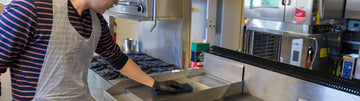 Kris wearing a disposable poly apron and cleaning a steel counter