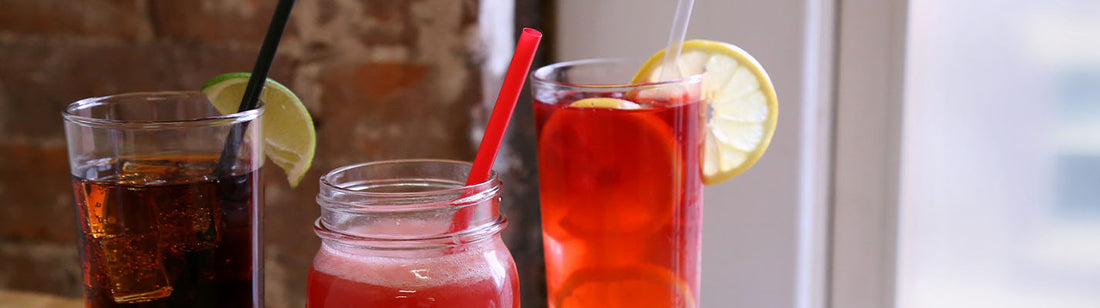 three cold drinks in glass cups with straws and garnishes