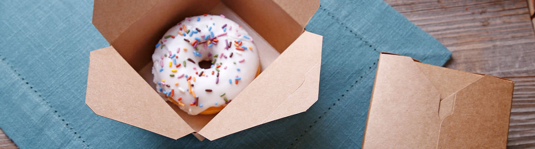 white sprinkle donut in a folded paper takeout box