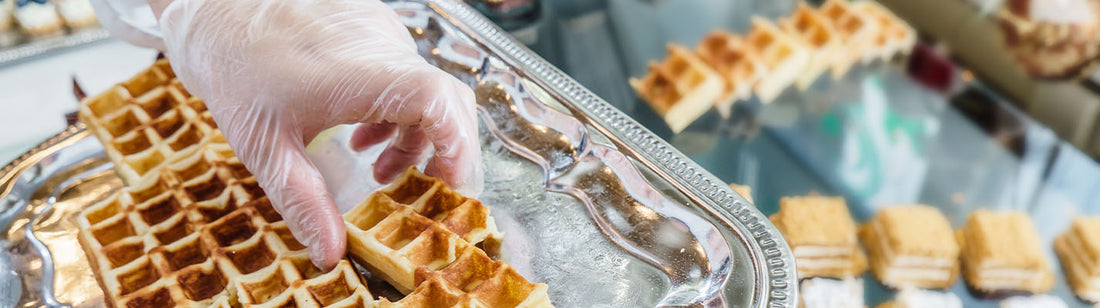 person wearing a vinyl glove and placing waffle bites on a silver tray