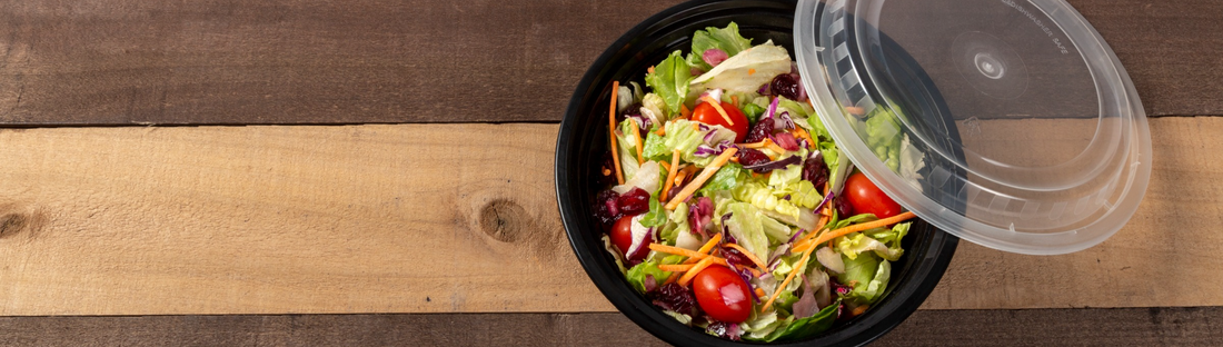 24 oz round black takeout container of fresh salad with clear lid to the side