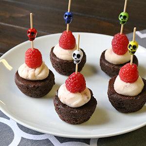 mini brownies with icing and a raspberry with skull picks through them