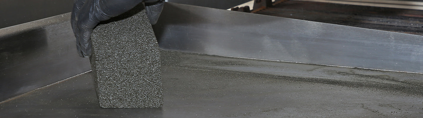 Jorge wearing a black nitrile glove and cleaning a steel surface with a big ol' grill brick