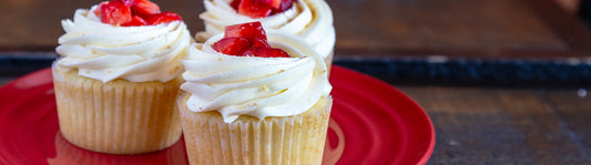 Red plate with three vanilla cupcakes with White icing and strawberries on top