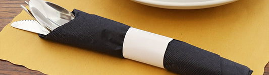 yellow placemat with silverware wrapped in a black napkin and held together by a white napkin band