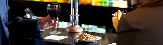 two people sitting at the bar with drinks and a bowl of peanuts