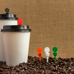Two white coffee cups in a pile of coffee beans with beverage plugs in cup lids and pile of beans