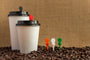 Two white coffee cups in a pile of coffee beans with beverage plugs in cup lids and pile of beans