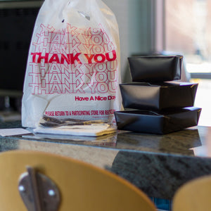 folded black takeout boxes next to a takeout bag