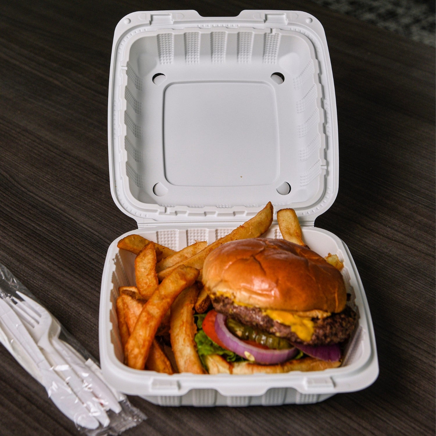 white 8" x 8" x 3" Lightweight Mineral Filled PP Vented Container with Hinged Lid open with a burger and fries inside on a table with cutlery kit to the side