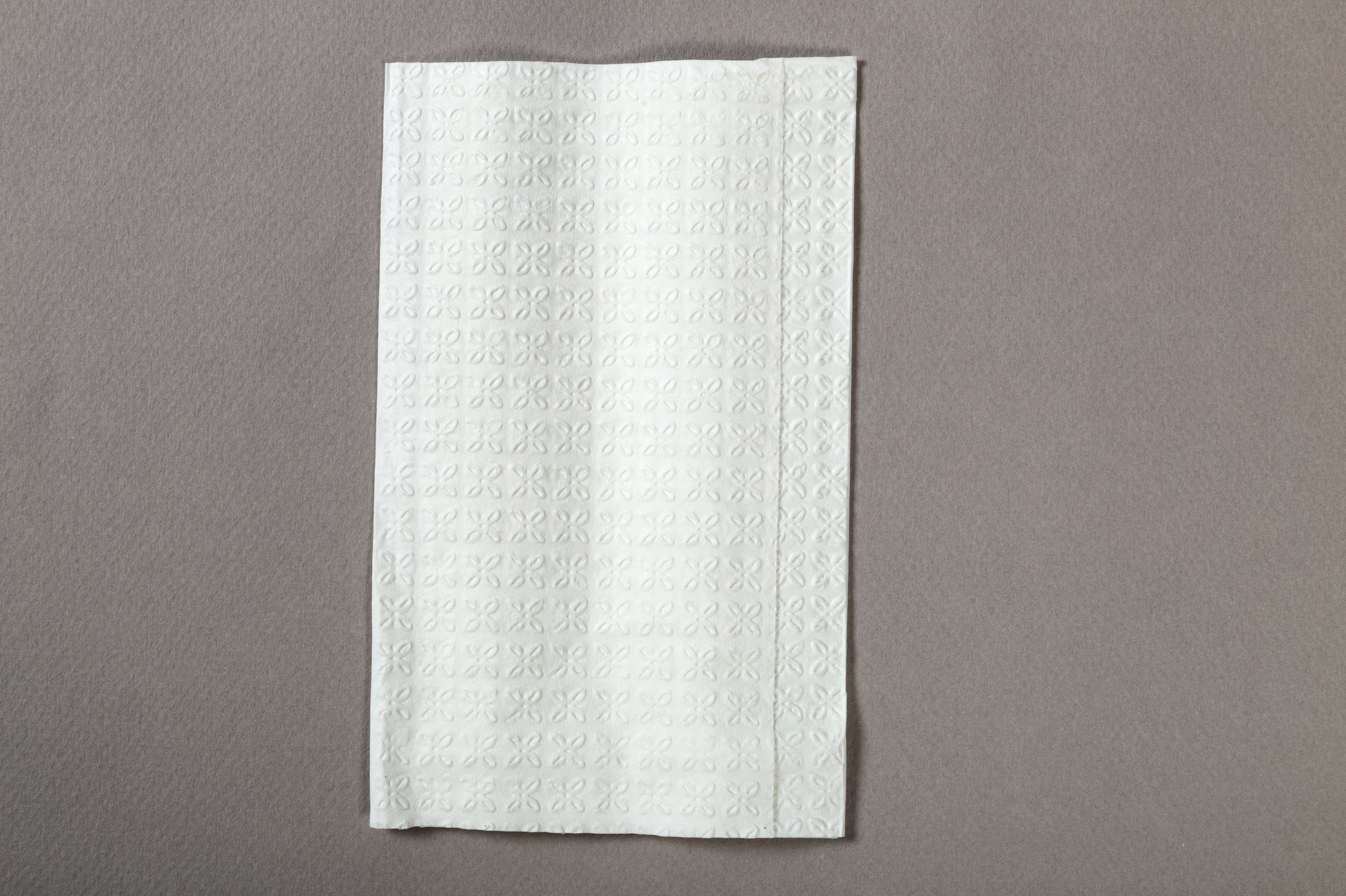 7.8" x 6.25" 2 Ply White Interfold Embossed Napkin on a grey counter