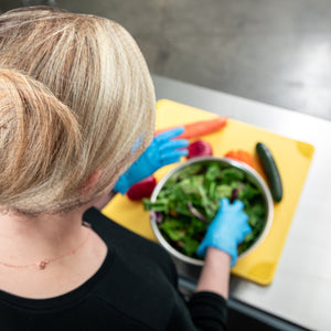 Person wearing a hairnet and prepping a salad