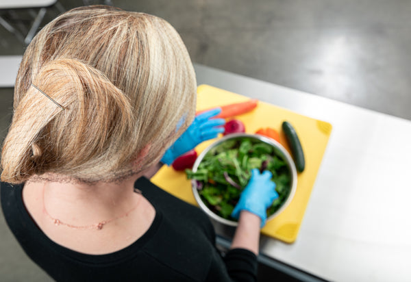 Person wearing a hairnet and prepping a salad