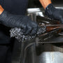 person wearing a black nitrile gloves and and scrubbing a stovetop with a with a Regular 35g Stainless Steel Sponge