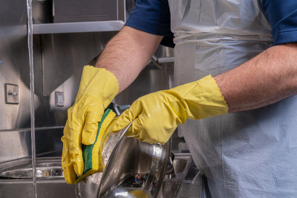 person wearing a yellow rubber glove and scrubbing a bowl with a Green 3.75