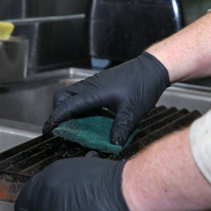 person wearing black nitrile gloves and scrubbing grill with Green 6