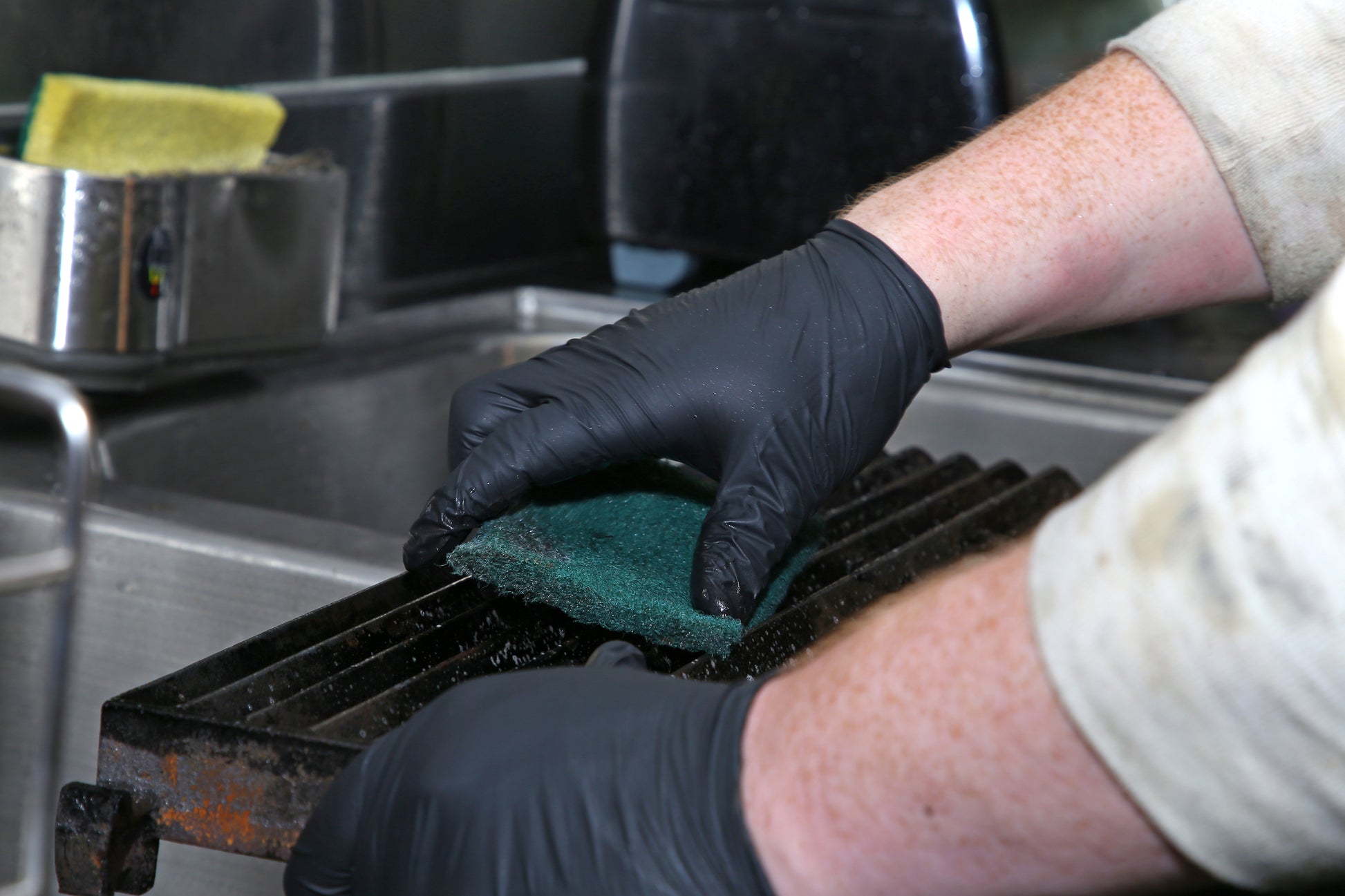 person wearing black nitrile gloves and scrubbing grill with Green 6" x 9" Heavy Duty Scouring Pad