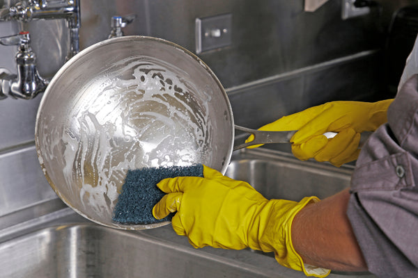 Person wearing yellow gloves and scrubbing metal dish with a Commander Blue 3.5