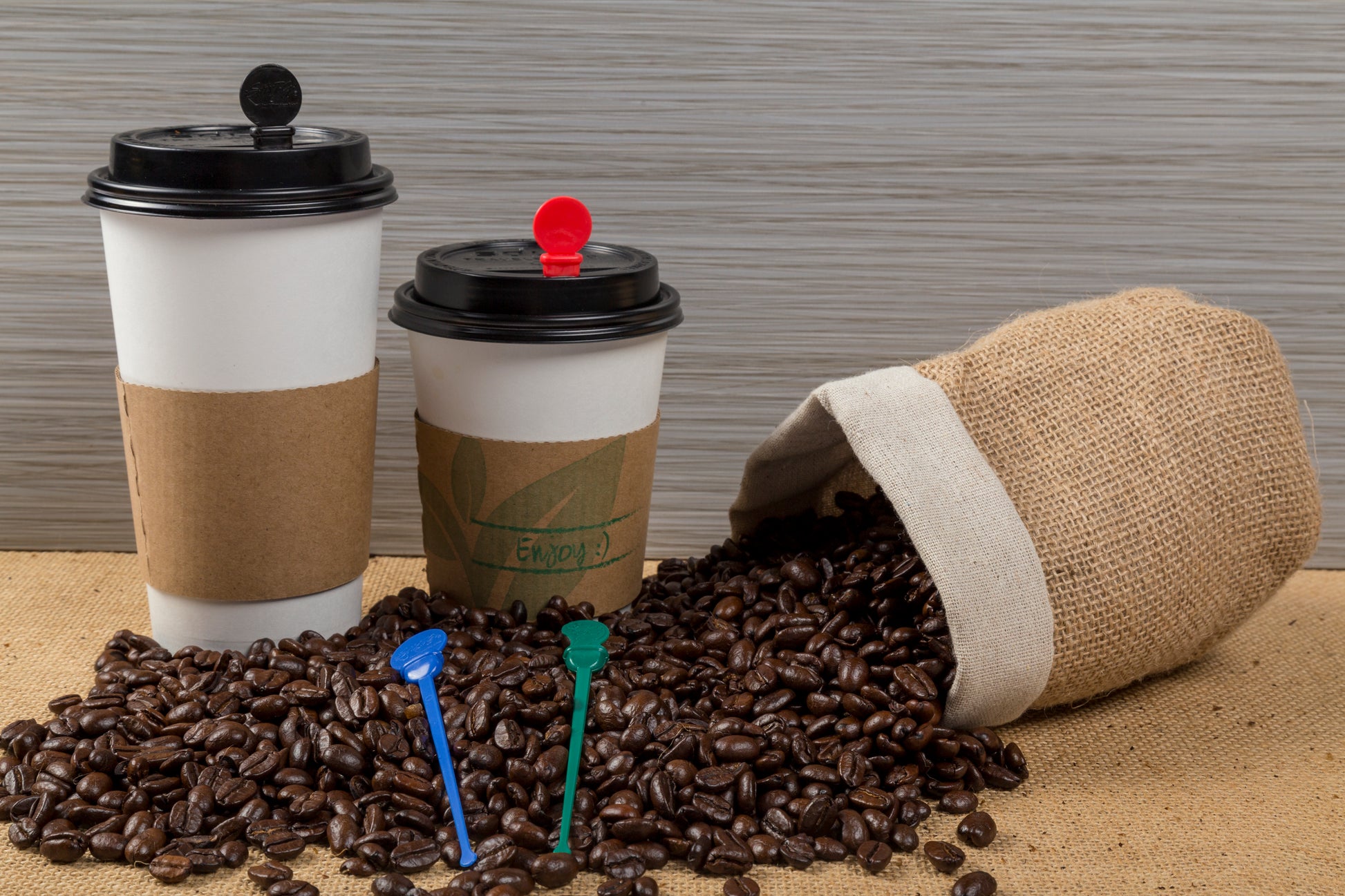 two white hot cups with cup sleeves on them, spilled back of coffee beans in front with 4.75" stir plugs