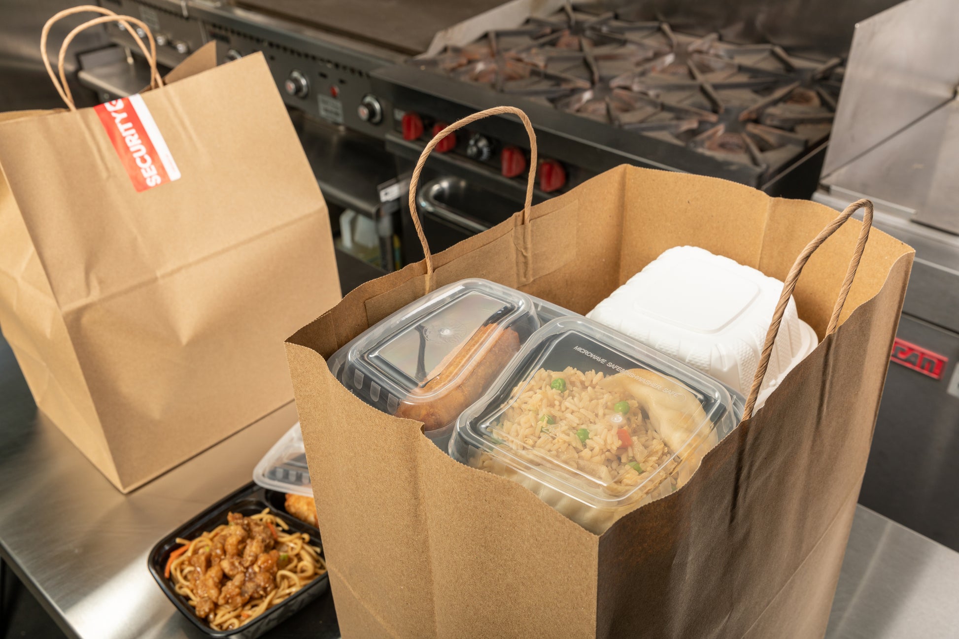 Chinese takeout dishes packed into a 12" x 9" x 15.75" Twisted Handle Kraft Paper Bag
