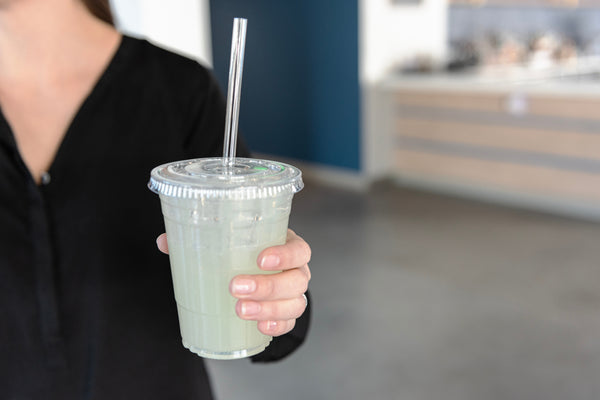 person holding up a lemonade in a clear cup with a clear compostable cellulosic straw