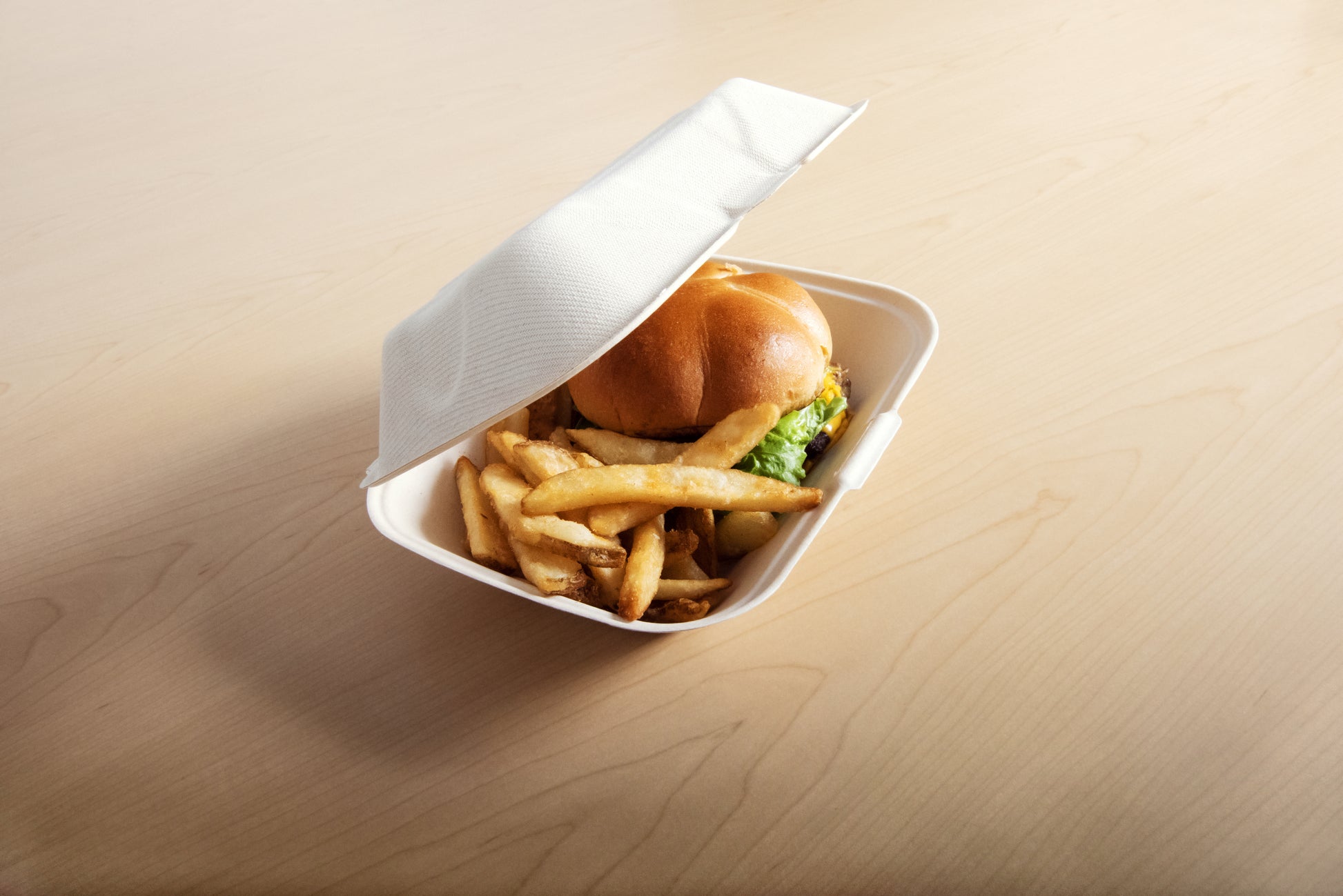 9" x 6" no added PFAS molded fiber hinged lid container partially open with burger and fries inside